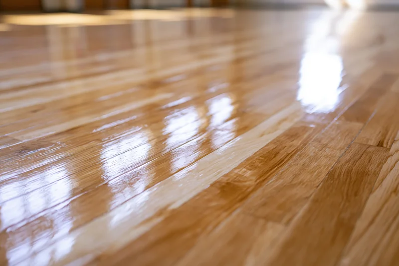Polished hardwood gymnasium floor stretching into the distance with reflective surface and wood grain texture