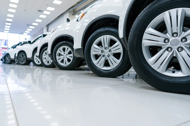 Row of white suvs lined up in a car dealership showroom with glossy tiled floor reflecting wheels and ceiling lights
