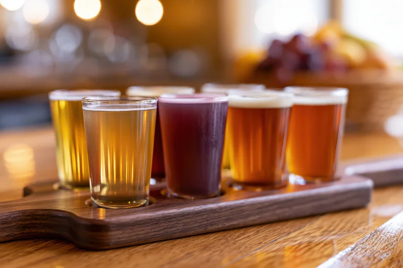 Six small glasses of craft beer arranged on a wooden tray on a bar counter