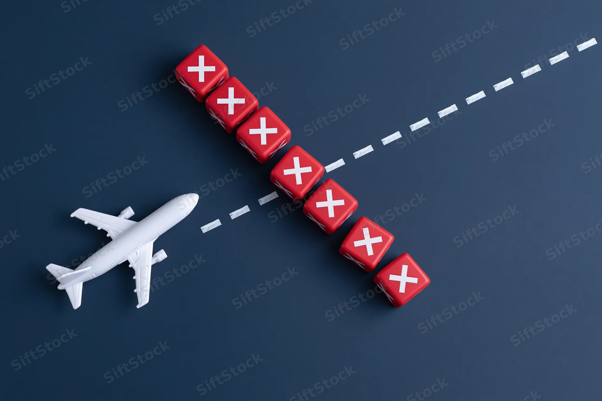 White toy airplane model next to red dice with x marks arranged along a diagonal dashed line on dark surface