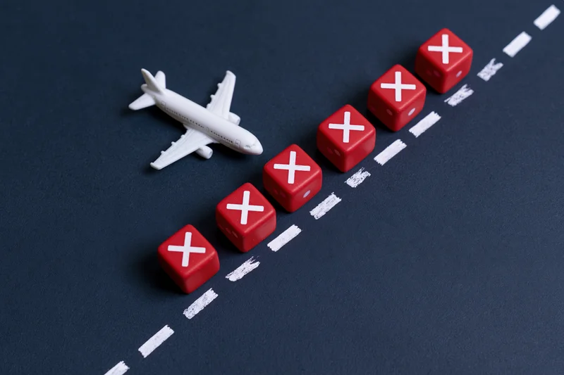 Small white airplane toy model next to red dice with x marks along a dashed white line on dark surface