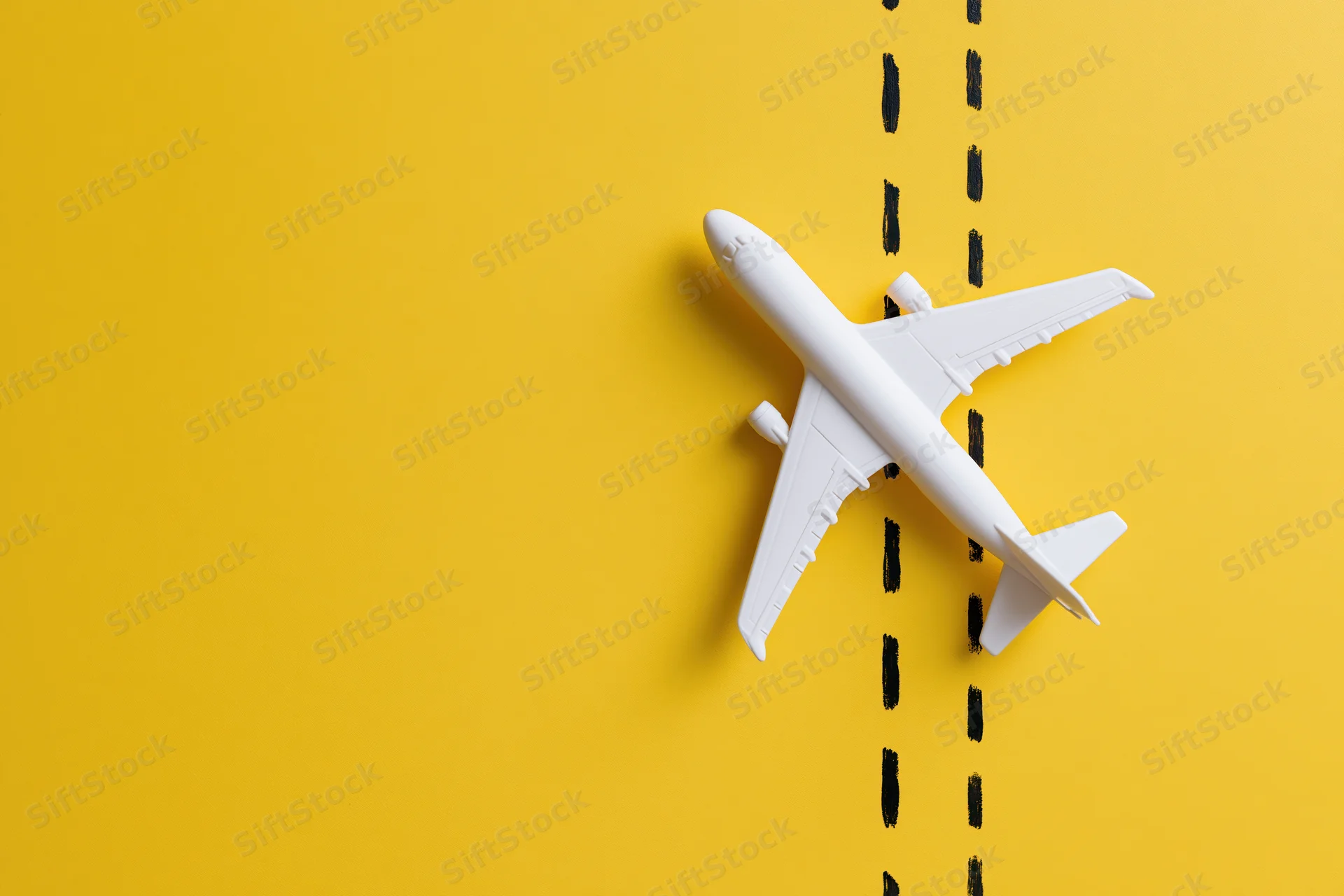 White plastic toy airplane placed flat on yellow background with black dashed line running through it