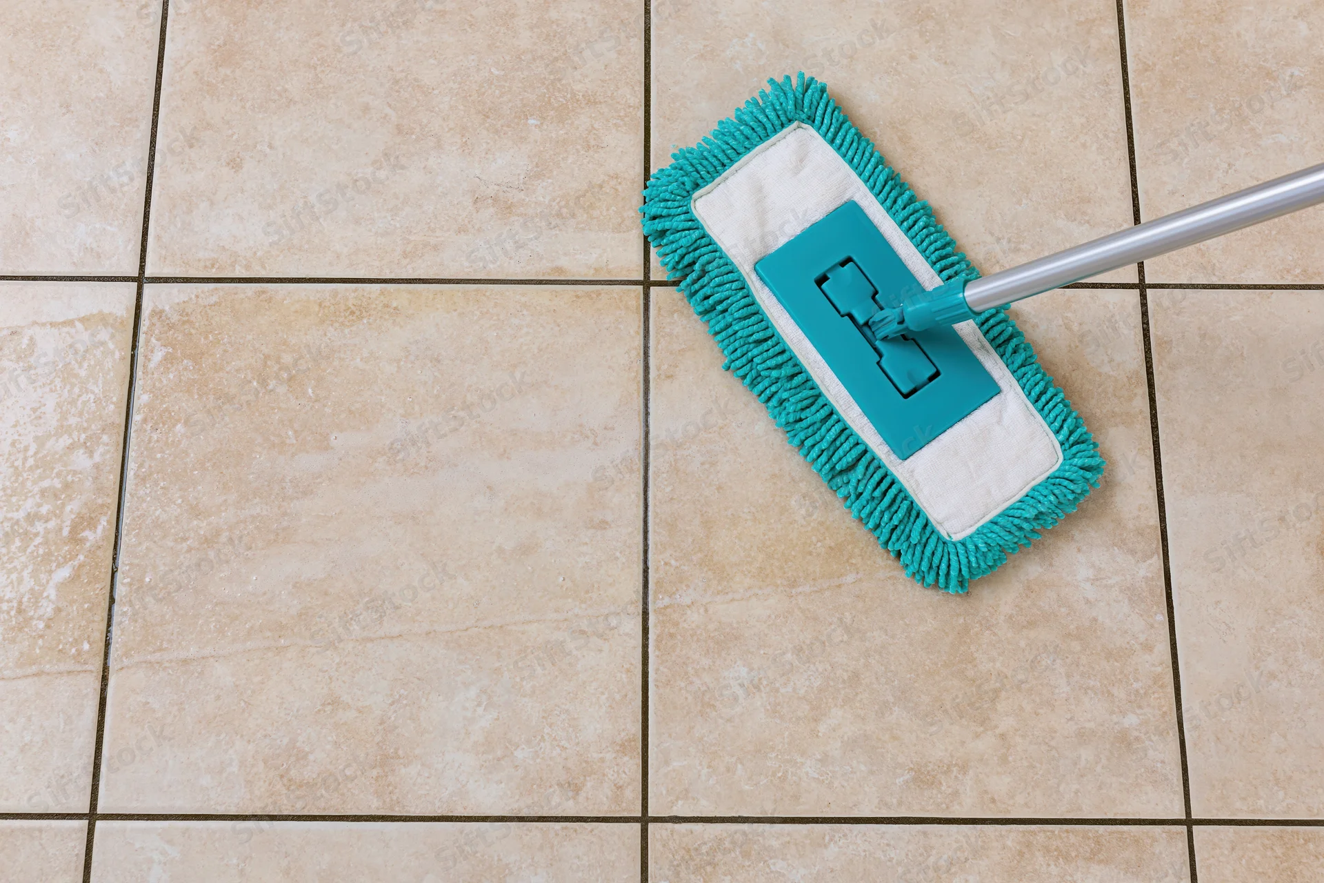 Teal microfiber flat mop cleaning beige tiled floor with visible grout lines