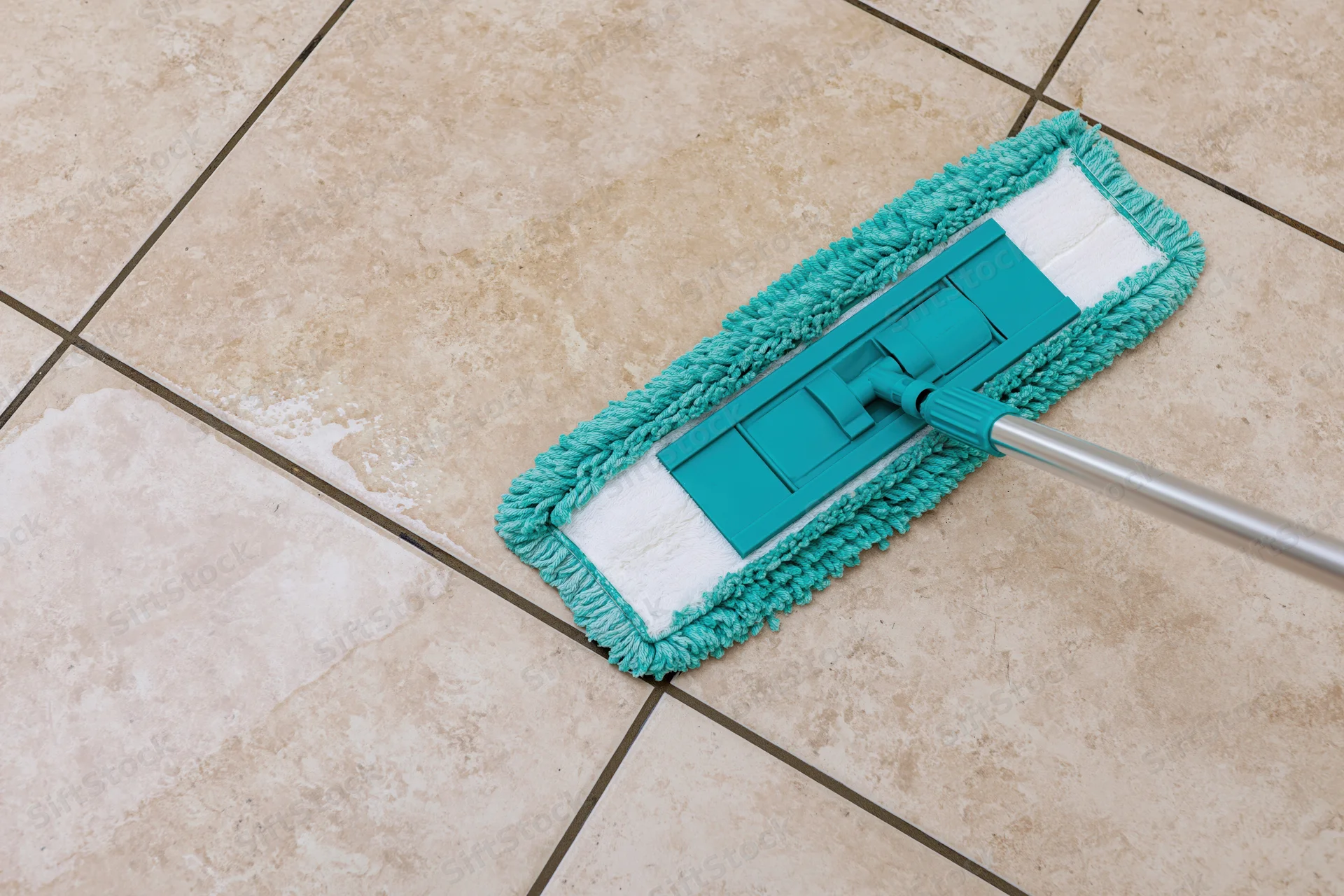 Teal microfiber flat mop cleaning tiled floor with visible grout and debris