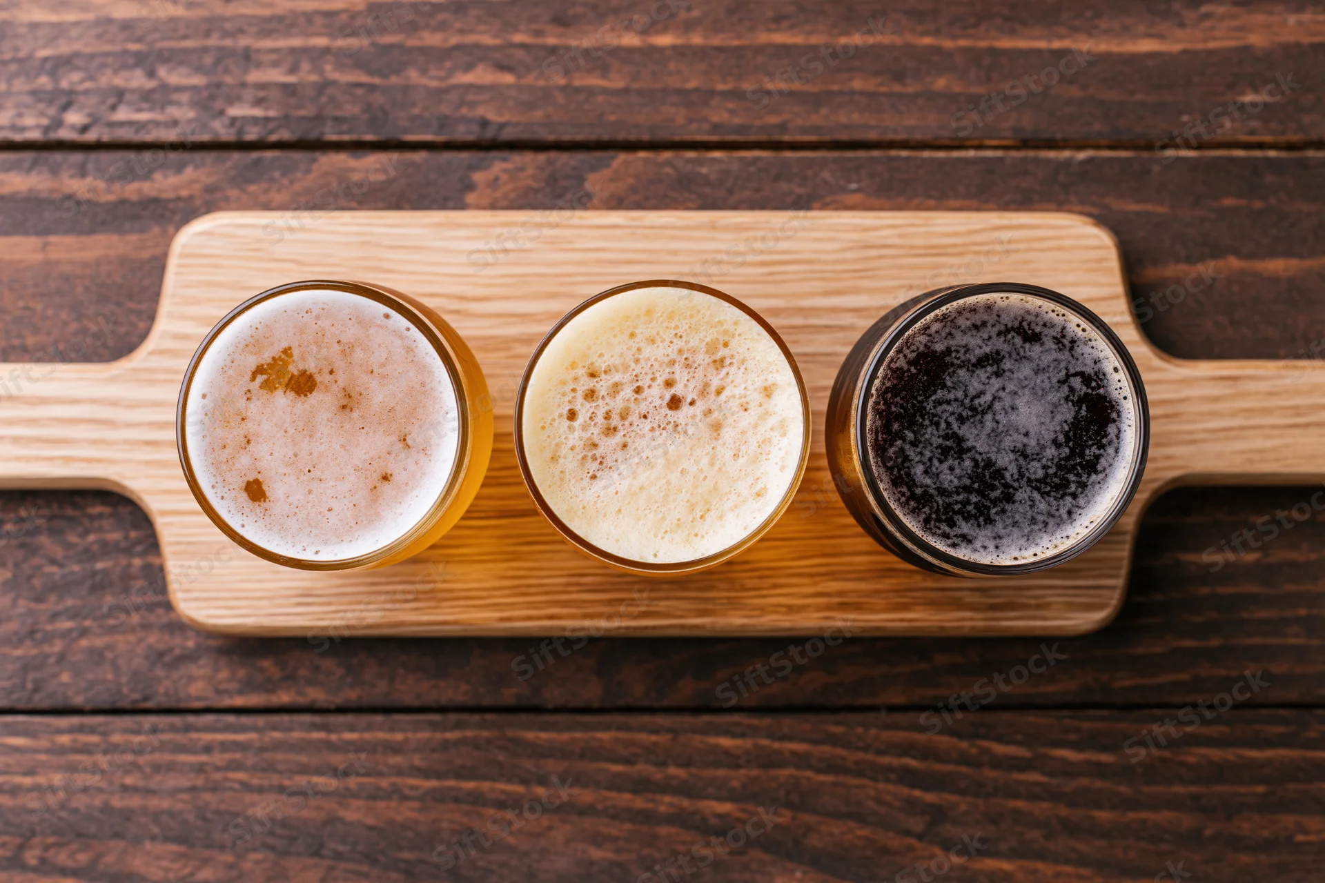 Three beer flight glasses arranged in a wooden paddle tray on a dark wood table