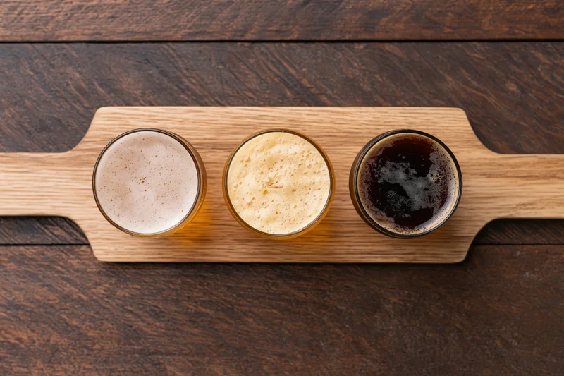 Three beer flight glasses arranged in a wooden paddle tray on a dark wood surface