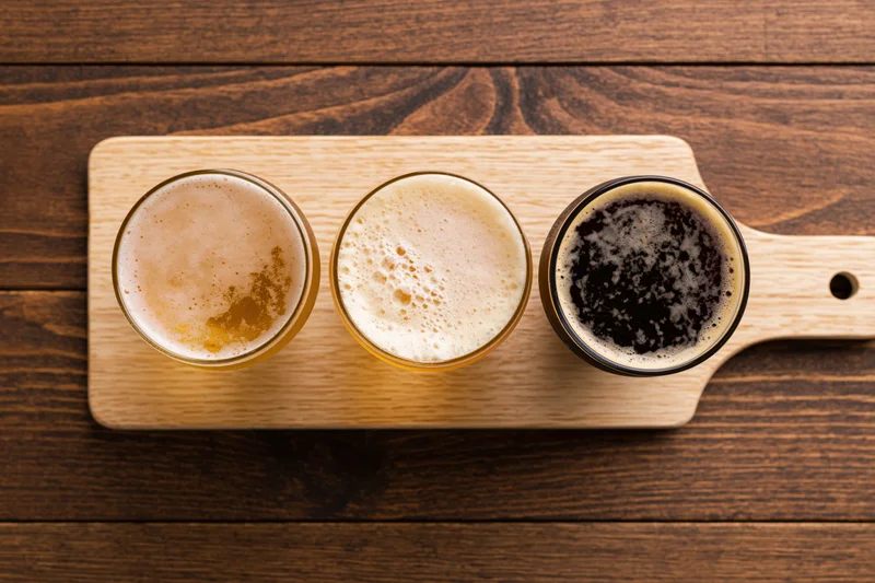 Three beer flight glasses arranged in a wooden paddle tray on a dark wood surface