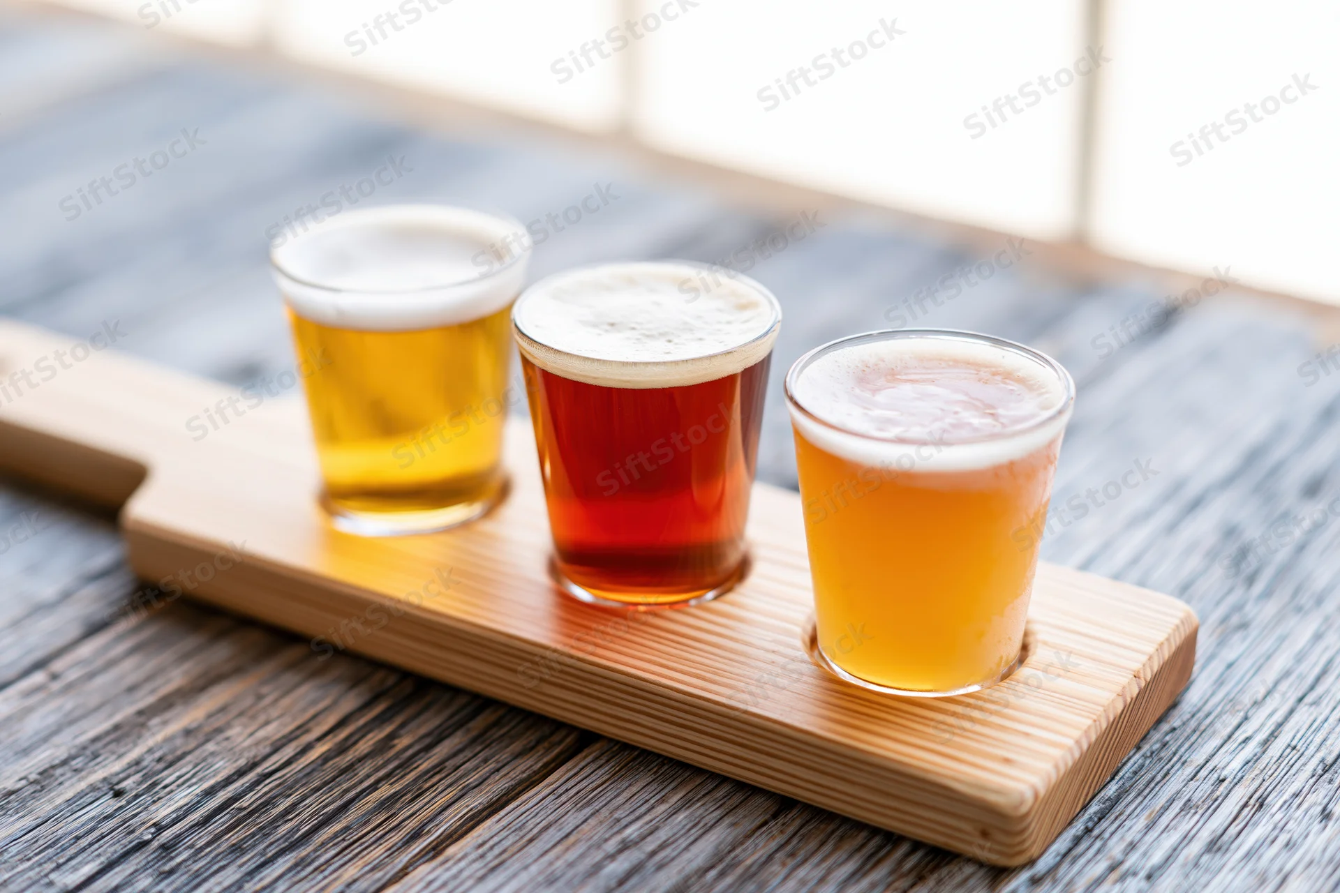 Three small beer tasting glasses arranged in a wooden flight paddle on a rustic wooden table