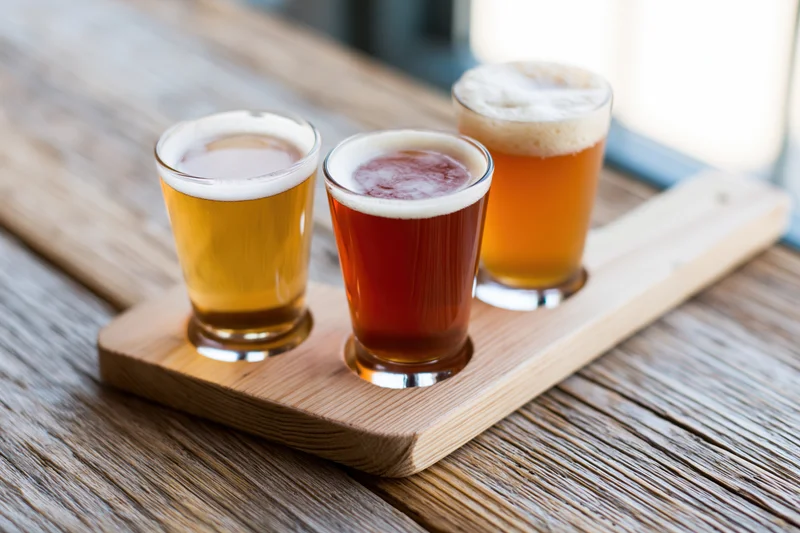 Three small beer tasting glasses arranged on a wooden flight paddle on a rustic table