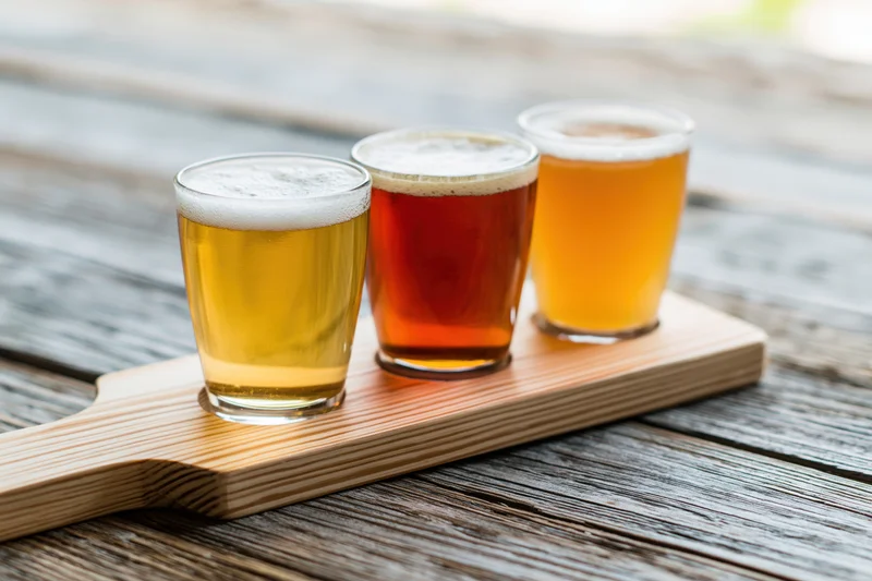 Three small beer tasting glasses arranged in a wooden flight paddle on a rustic wooden table