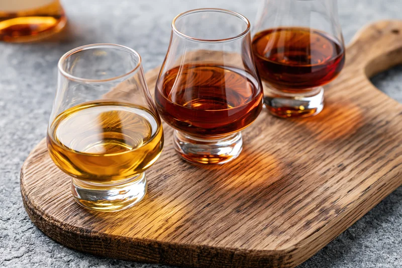 Three snifter glasses filled with amber spirits arranged on a wooden board