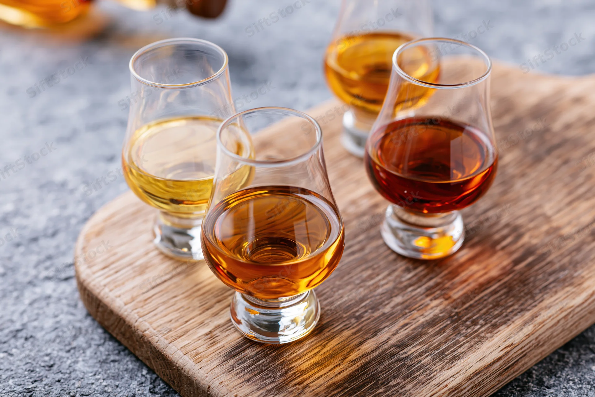 Three snifter glasses filled with amber spirits arranged on a wooden board