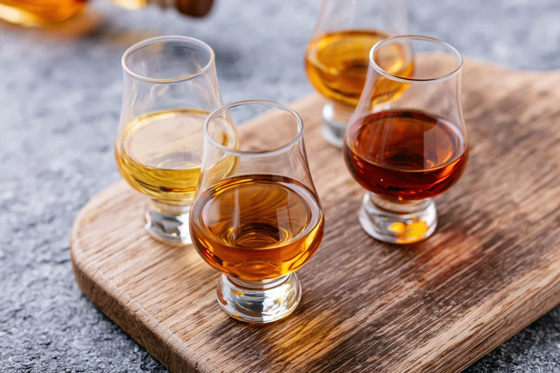 Three snifter glasses filled with amber spirits arranged on a wooden board