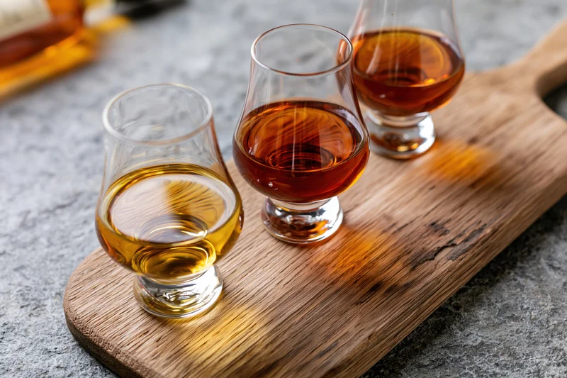 Three snifter glasses filled with amber spirits arranged on a wooden board