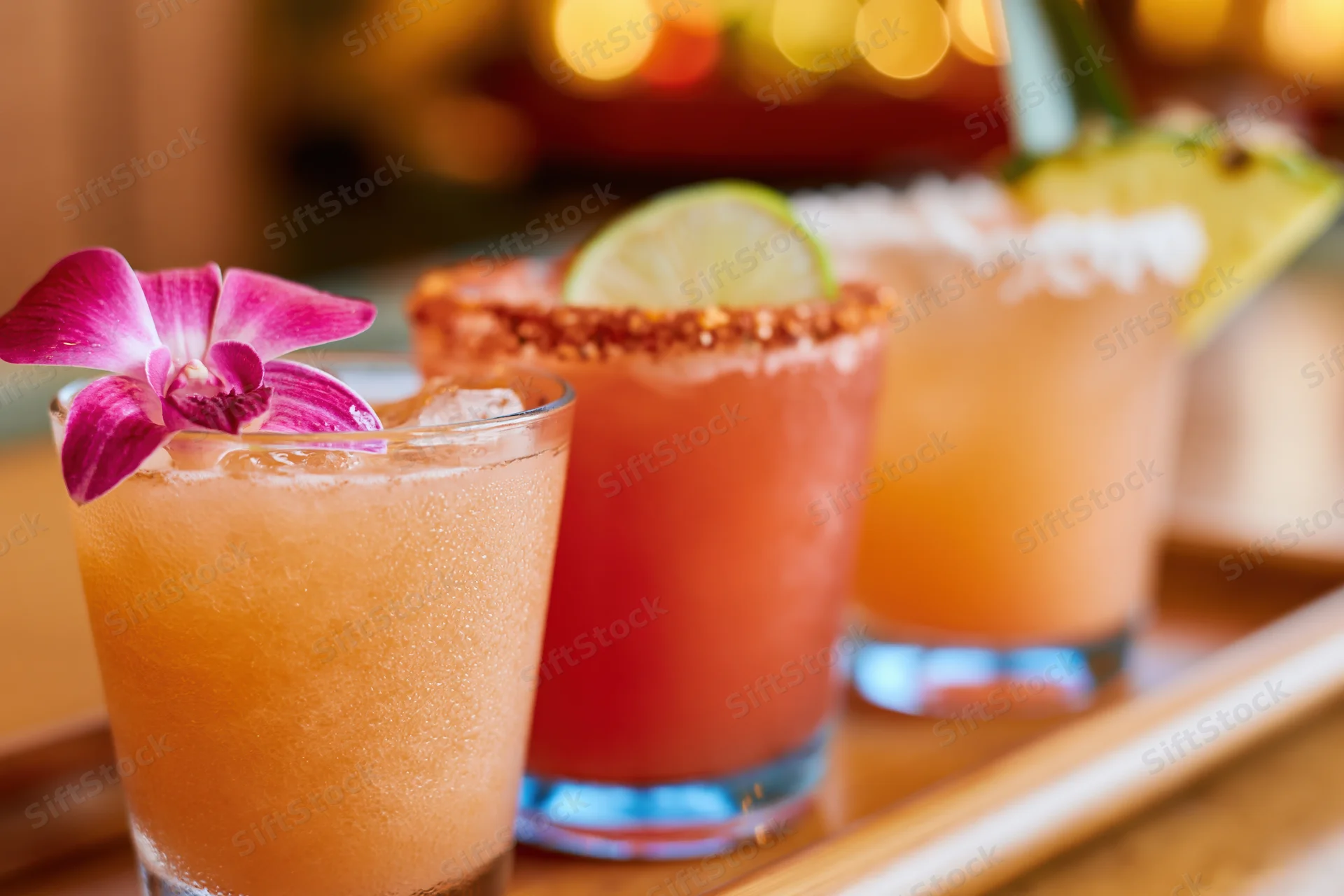 Three tropical cocktails garnished with lime and flower arranged on a wooden tray