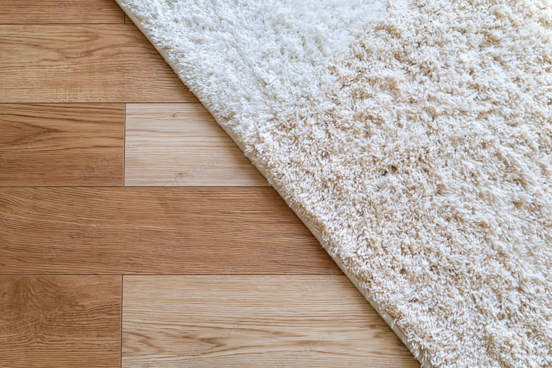 Warm oak laminate flooring meeting a beige shag rug in a corner of a room
