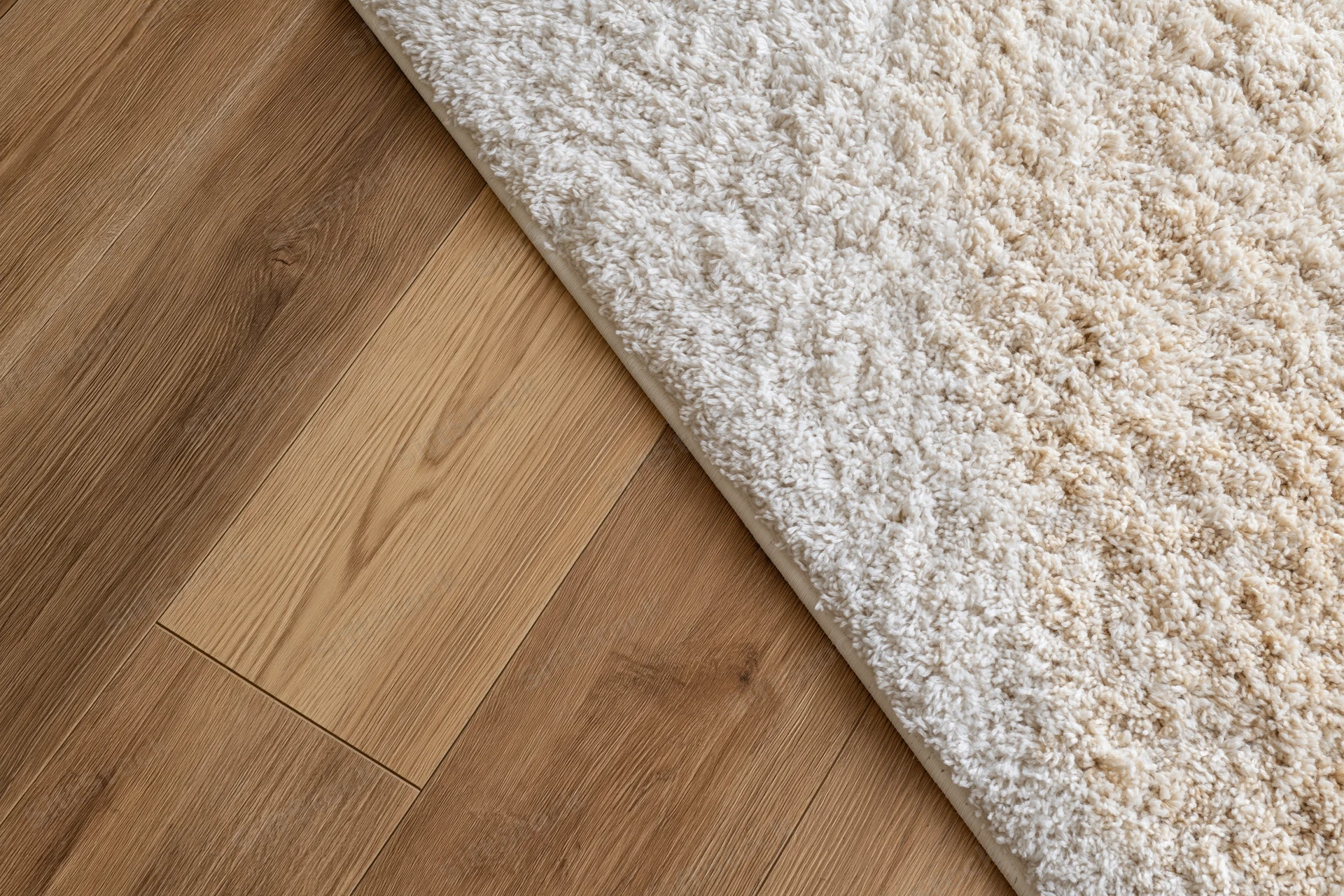 Warm oak laminate flooring meeting a beige shag rug in a home interior corner