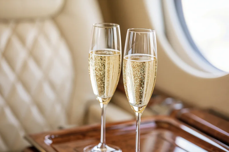 Two champagne flutes filled with sparkling wine on a wooden tray inside a private jet cabin
