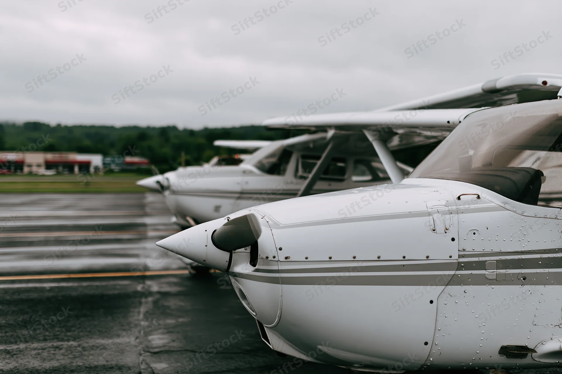 Two small single-engine propeller planes parked in a row on a wet tarmac at an airport