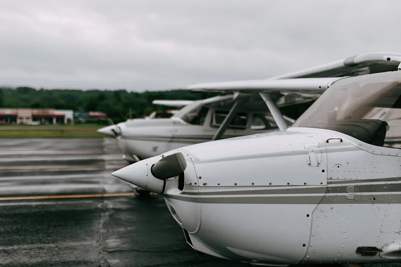 Two small single-engine propeller planes parked in a row on a wet tarmac at an airport