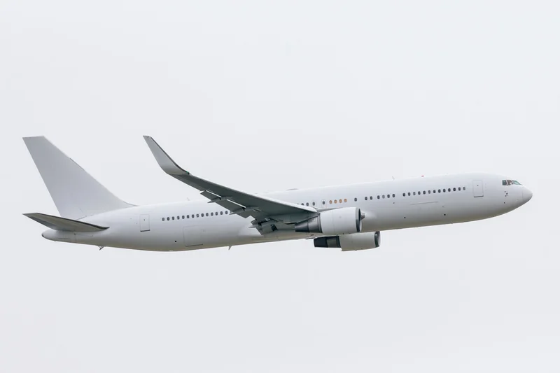 White unpainted commercial passenger jet in level flight side view against overcast sky