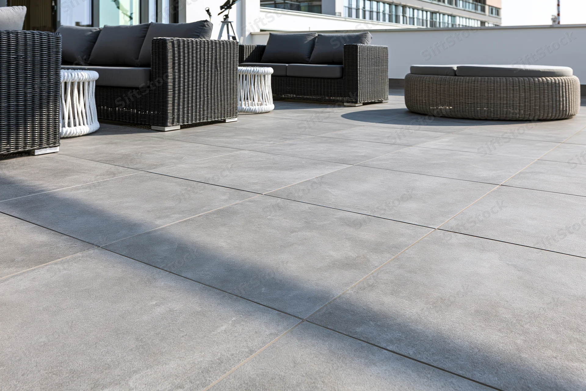 Dark wicker sofas and white tables arranged on a gray tiled rooftop terrace