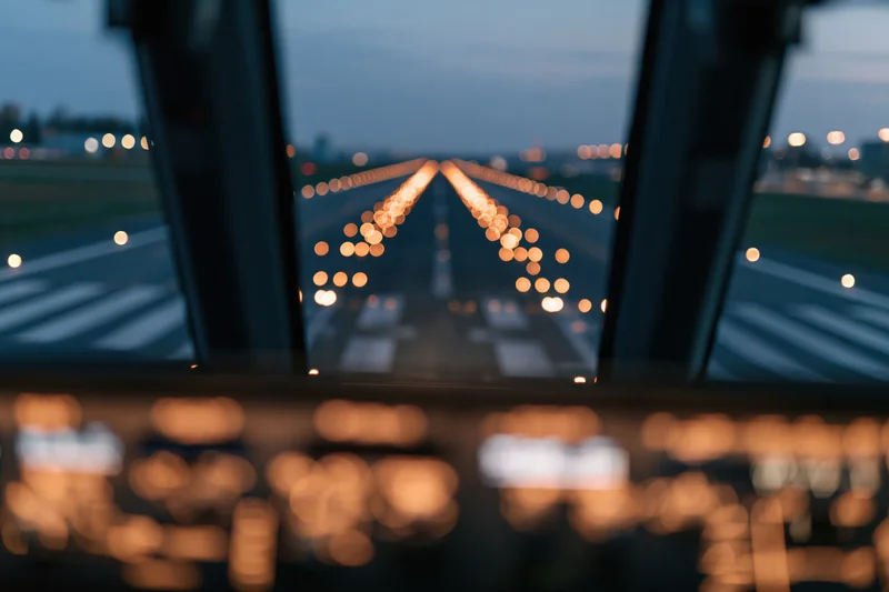 View through aircraft cockpit windshield during runway approach at dusk
