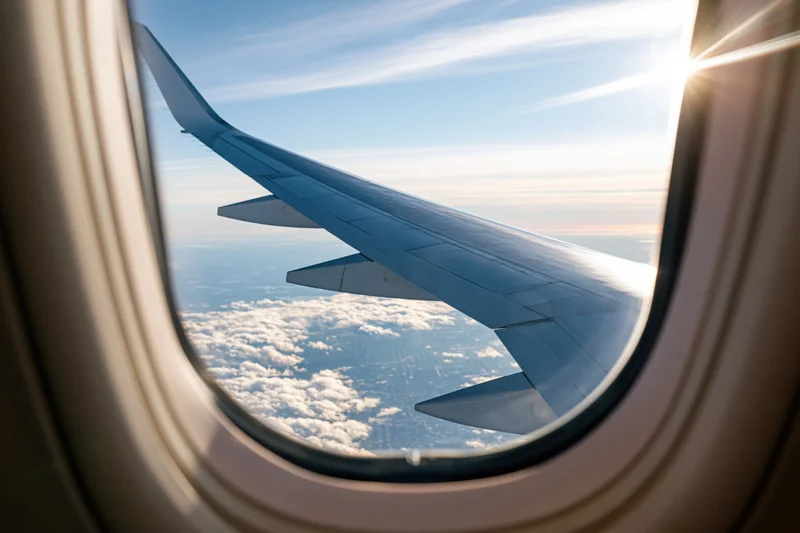 View through airplane window showing wing and clouds below during daytime flight