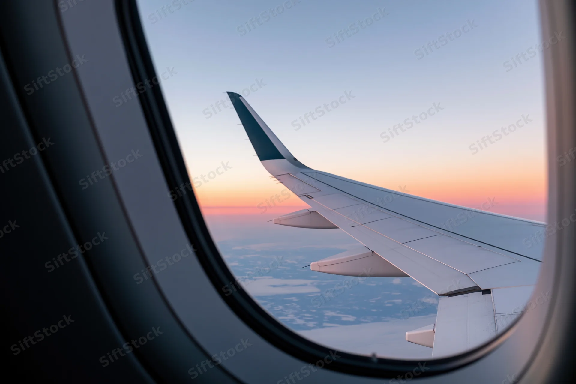 View through airplane window showing wing against sunset sky