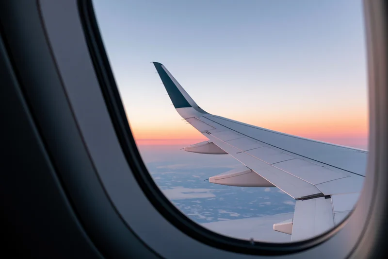 View through airplane window showing wing against sunset sky