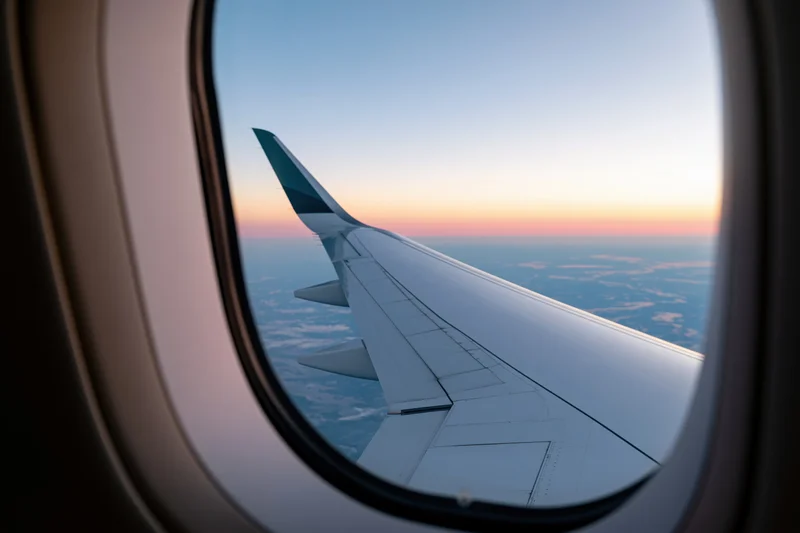 Airplane wing visible through oval window during sunset flight above clouds