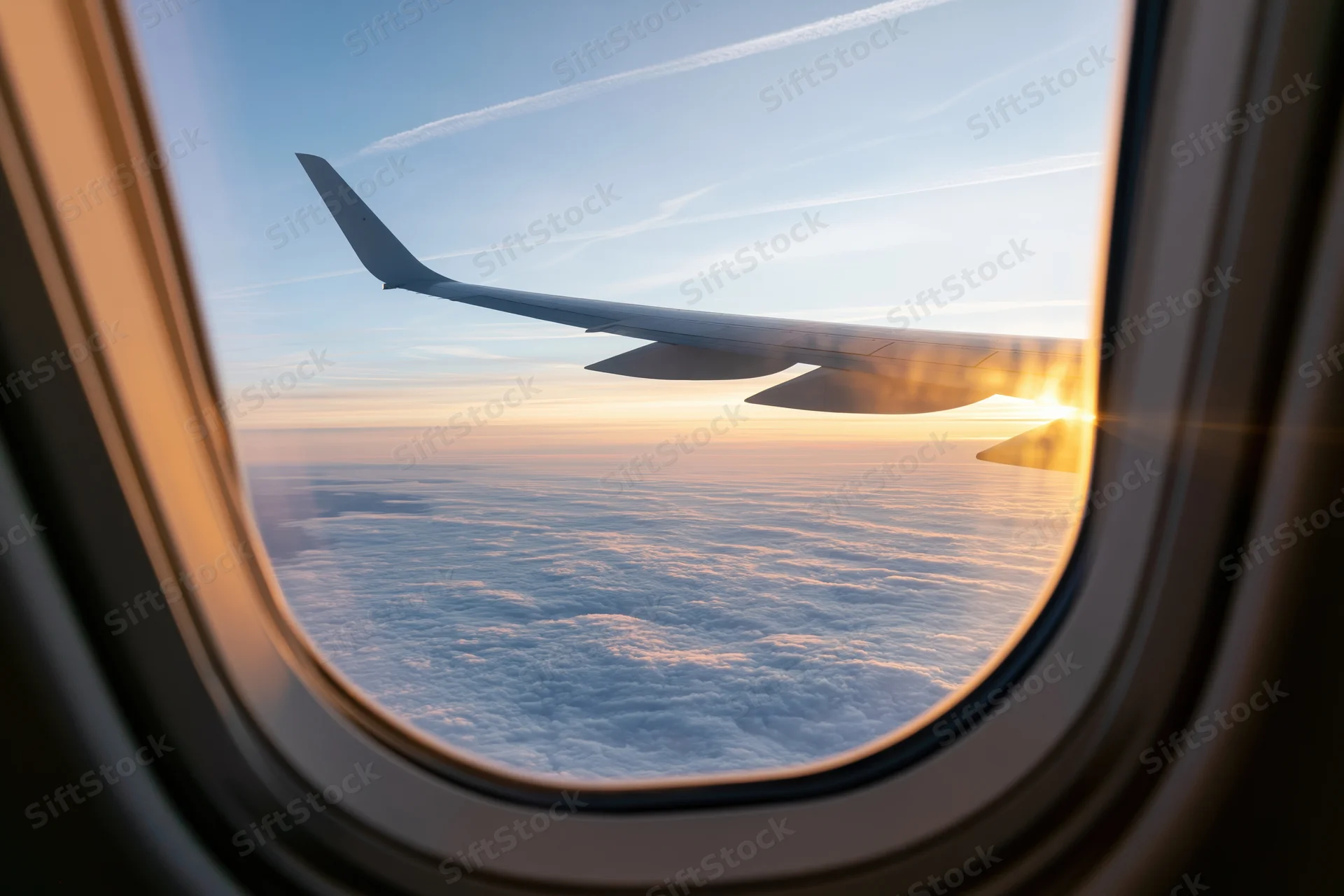 View through airplane window showing wing above clouds at sunset