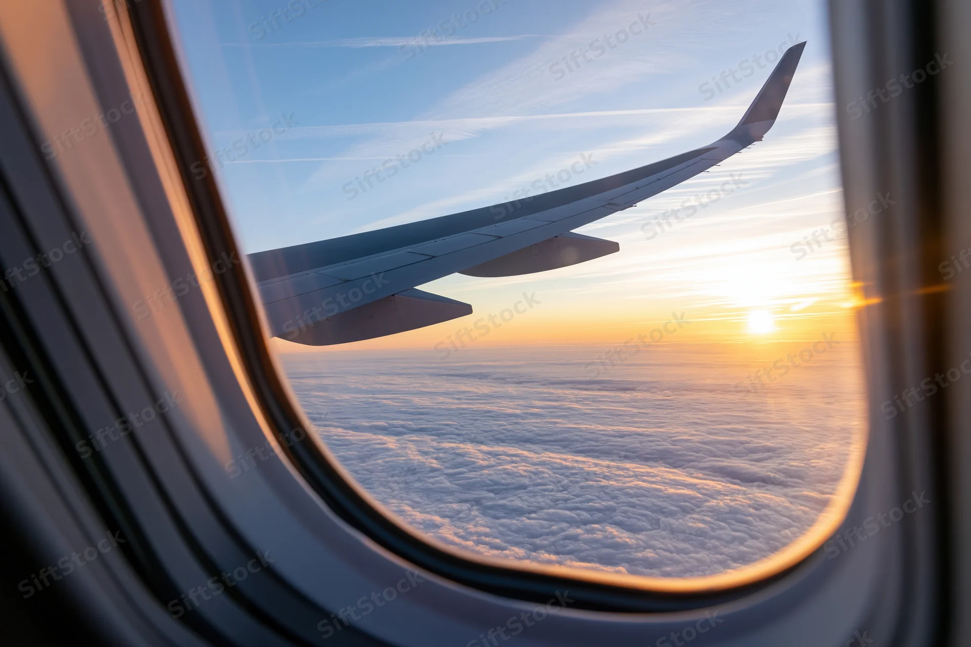 Airplane wing visible through window above clouds during sunset flight