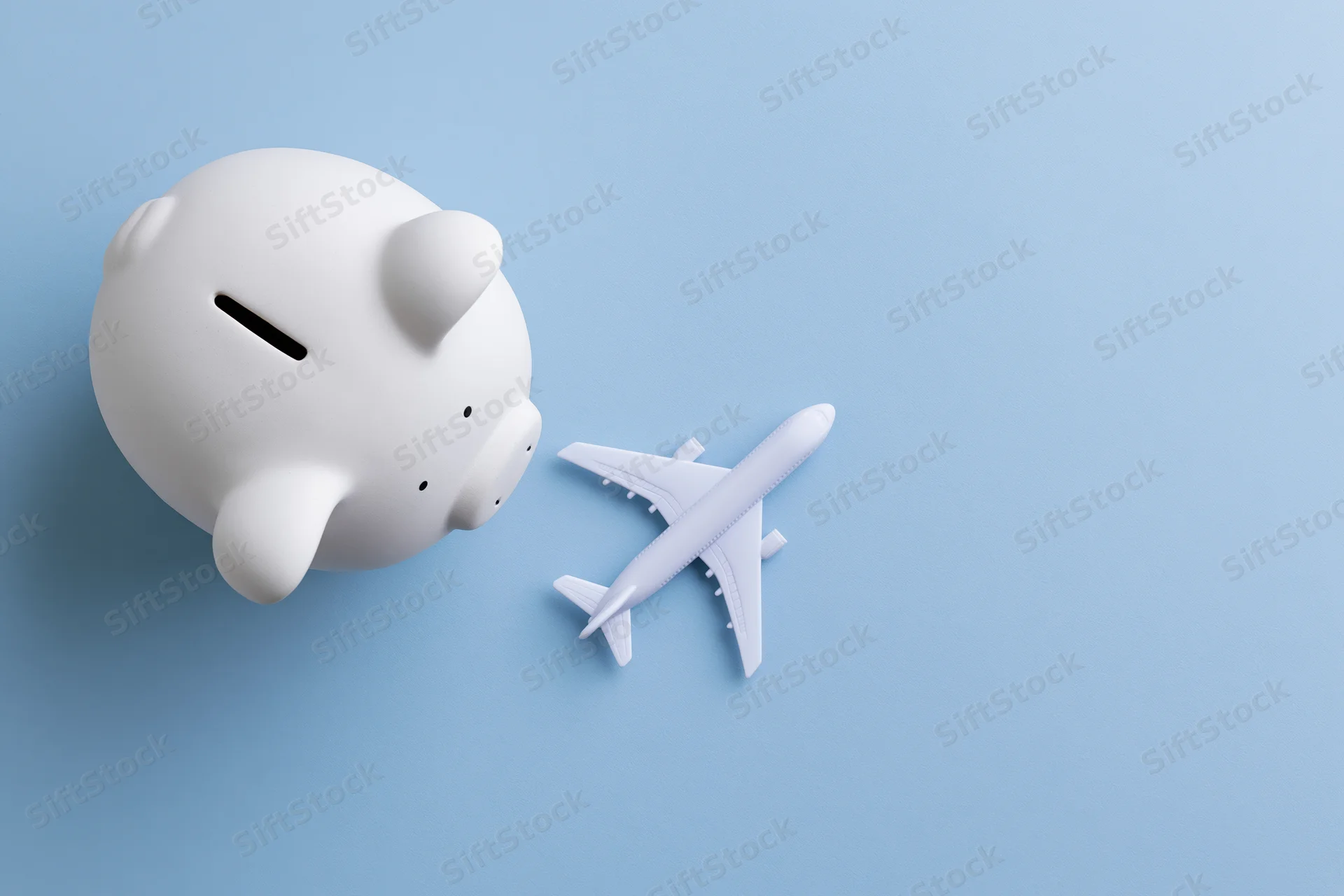 White ceramic piggy bank next to a white airplane model on a blue surface viewed from above