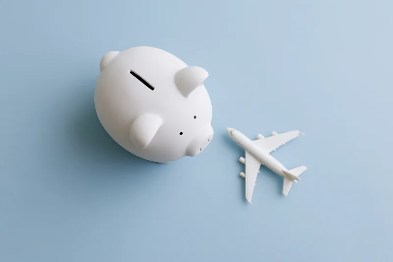 White ceramic piggy bank and toy airplane arranged on blue background viewed from above