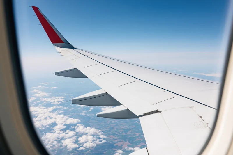 Airplane wing with red wingtip seen through window above clouds