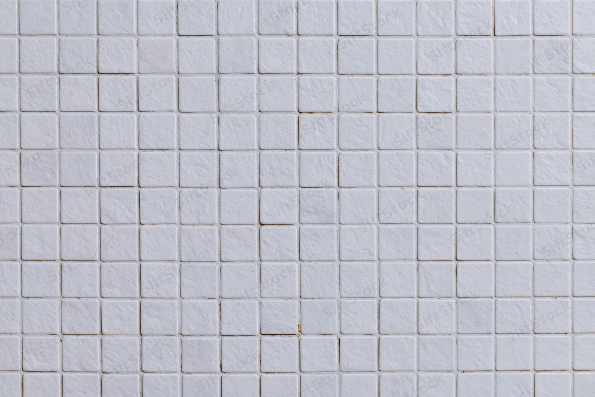White small square mosaic tiles arranged in a grid pattern covering a wall surface