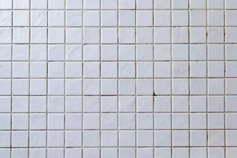 White square mosaic tile wall surface filling the frame with visible grout lines and minor discoloration