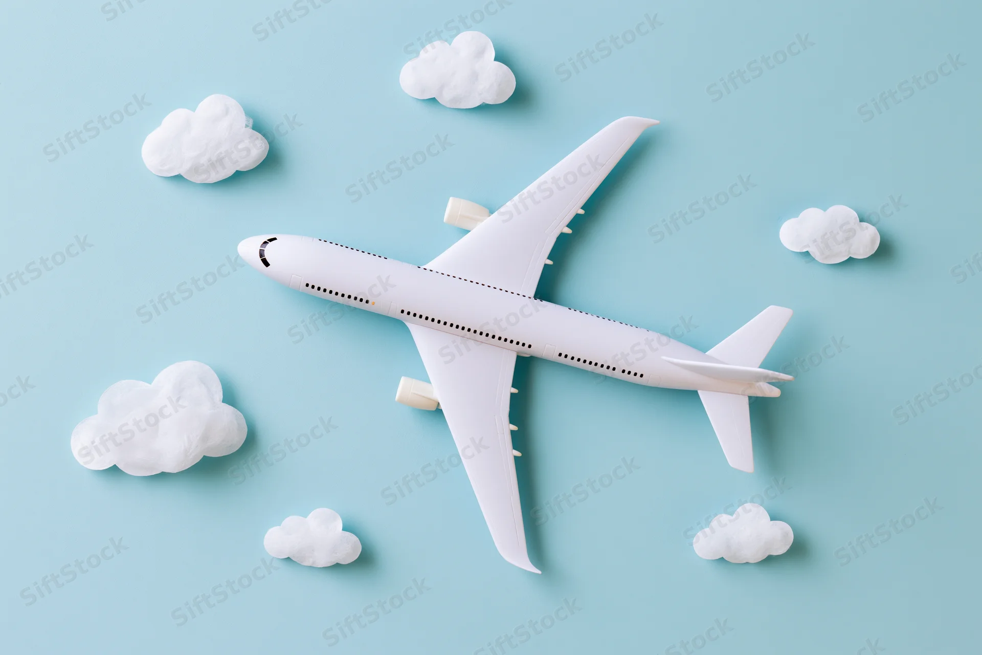 White toy passenger airplane model flying among clouds on light blue background