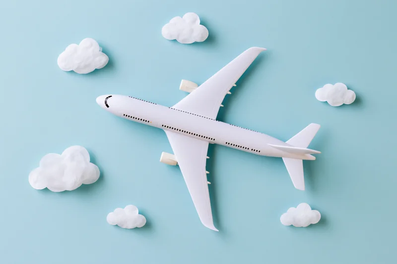 White toy passenger airplane model flying among clouds on light blue background