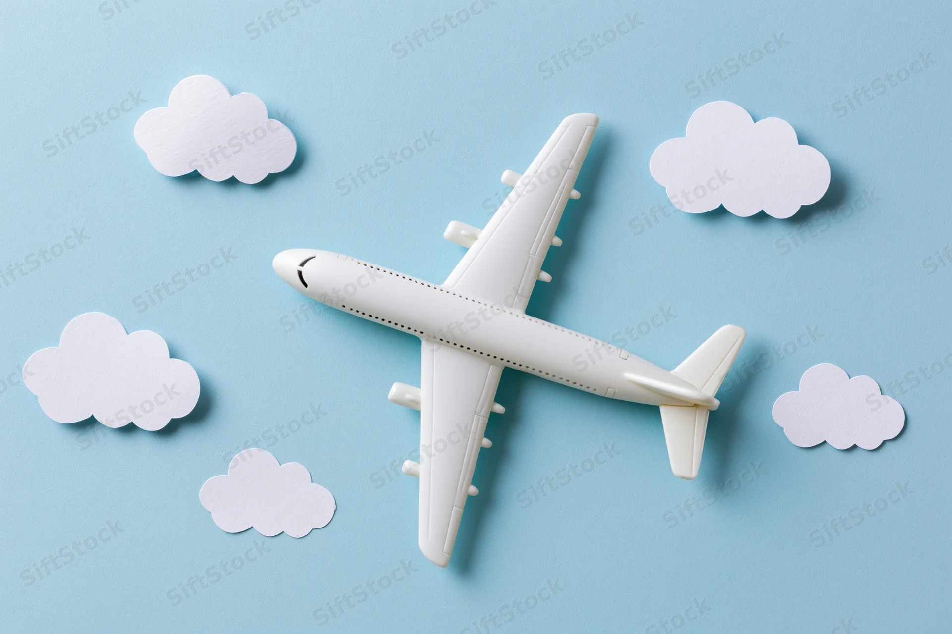 White toy passenger airplane model arranged on light blue surface with paper cloud cutouts around it