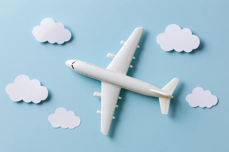 White toy passenger airplane model arranged on light blue surface with paper cloud cutouts around it