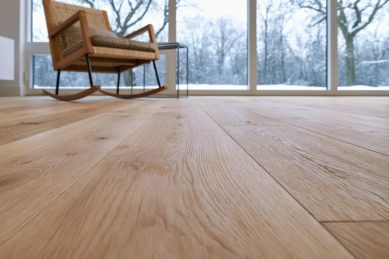 Wide-plank oak hardwood floor filling foreground with rocking chair and snowy view through large windows in modern living room