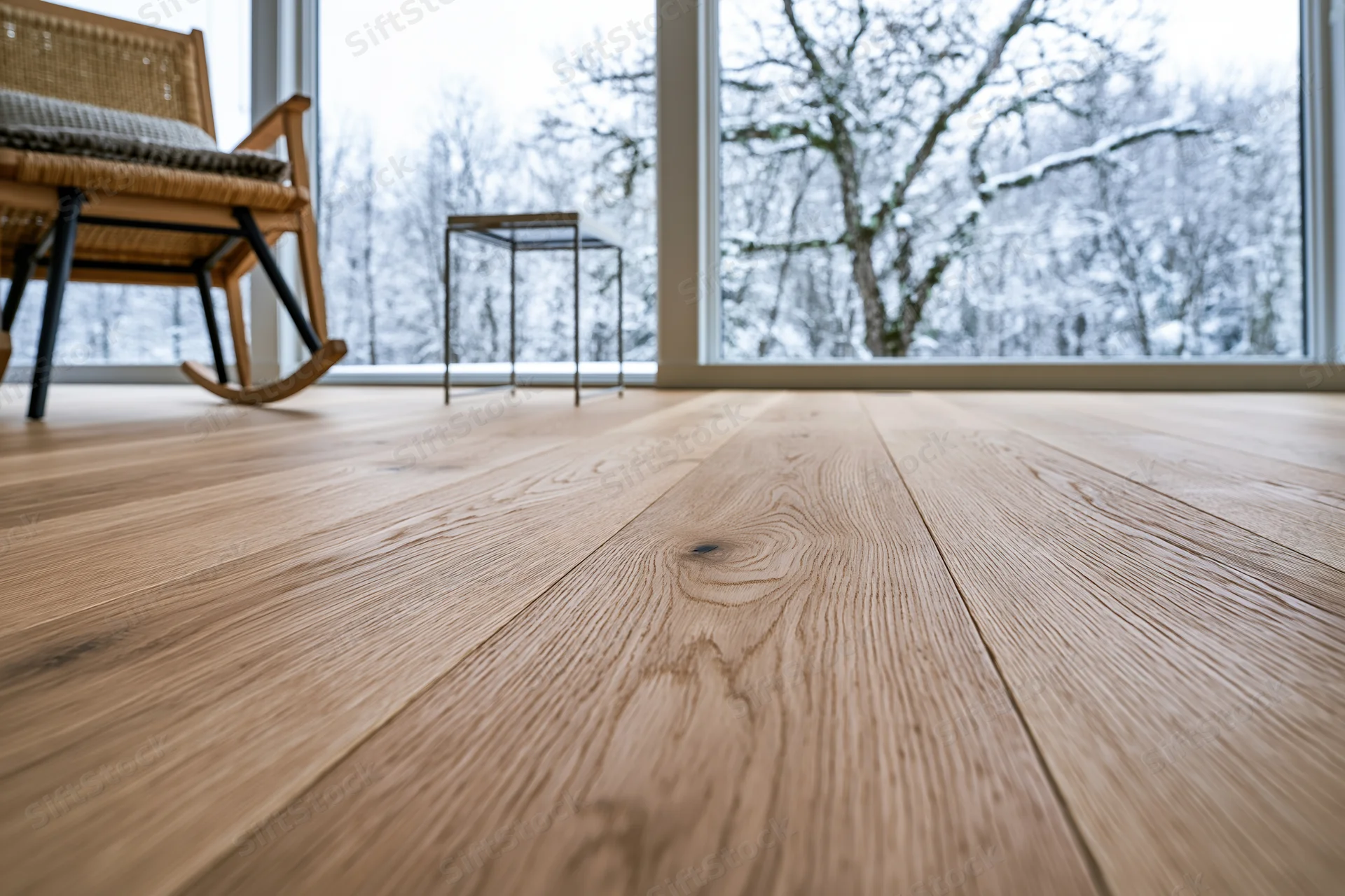 Wide-plank oak hardwood floor filling the foreground with a snowy winter landscape visible through large windows in a modern living room interior