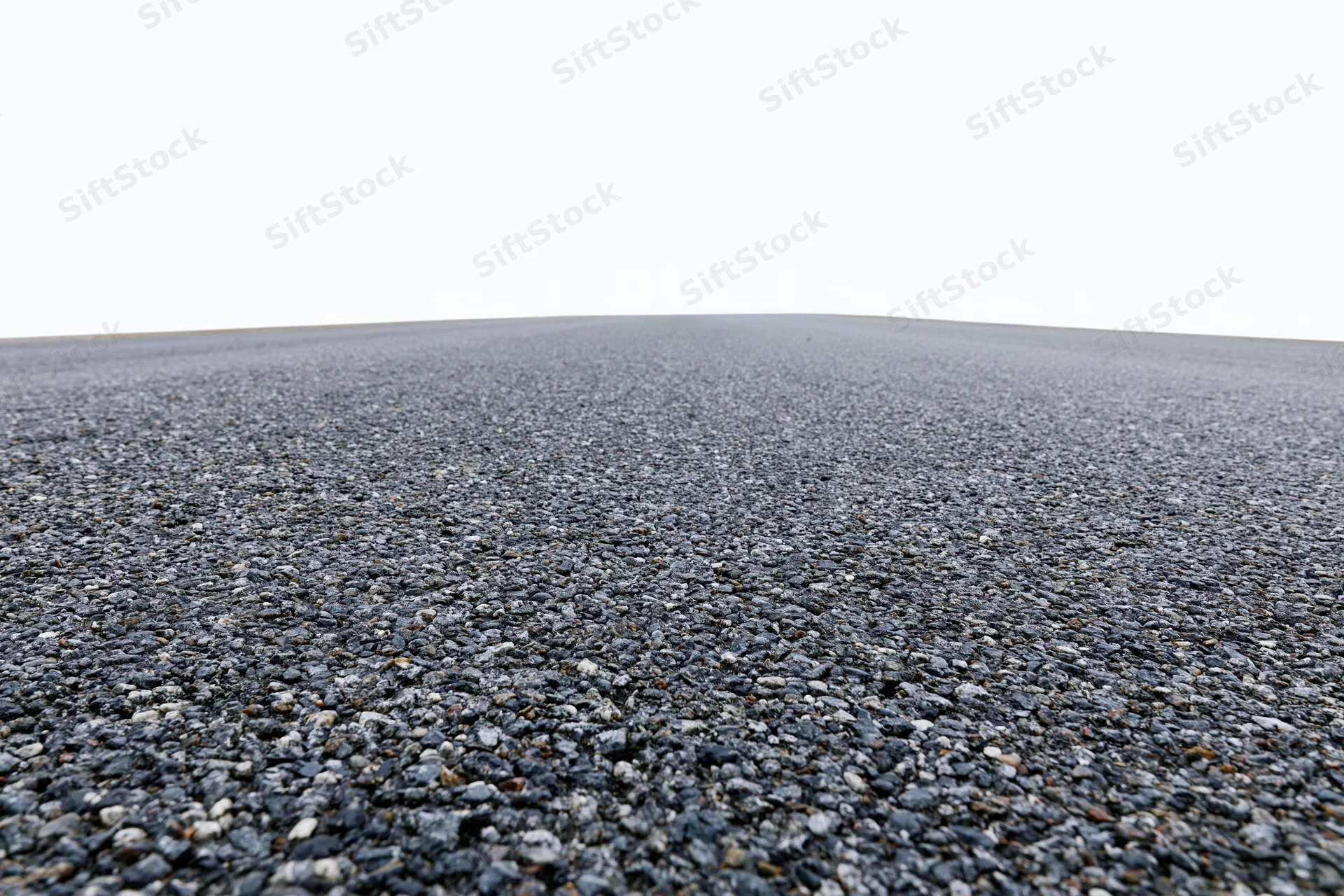 Flat asphalt surface stretching into the distance under a white sky, viewed from a low angle