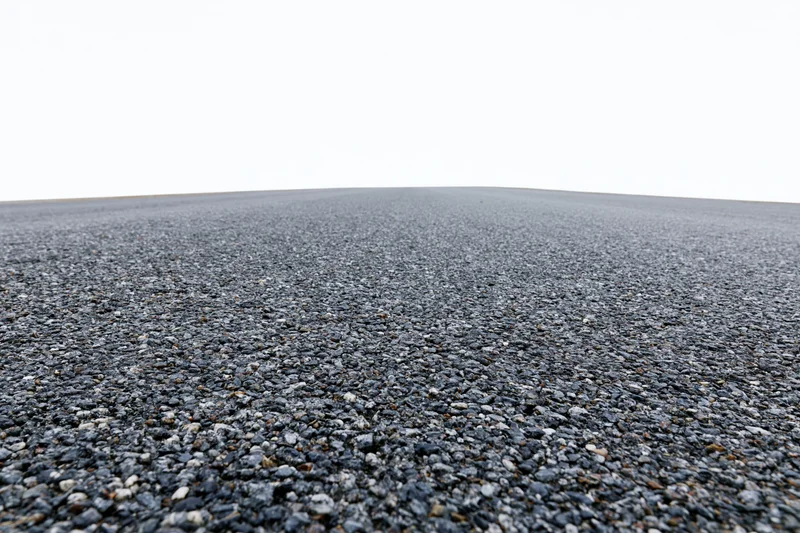 Flat asphalt surface stretching into the distance under a white sky, viewed from a low angle