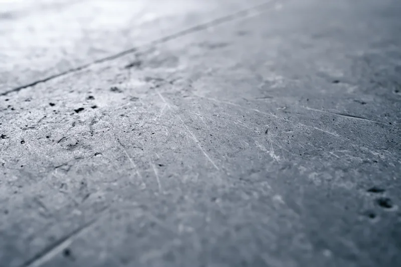 Worn concrete floor surface viewed diagonally with visible scratches and debris