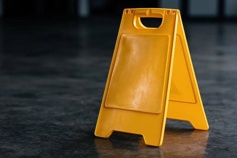 Yellow plastic a-frame caution sign standing alone on dark floor