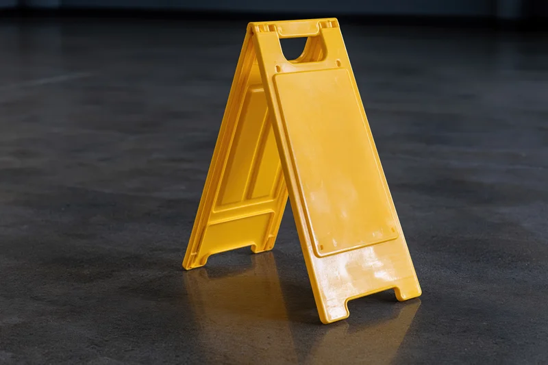 Yellow plastic a-frame caution sign standing upright on concrete floor