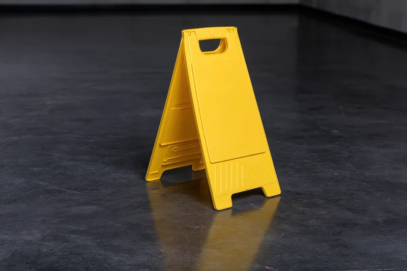 Yellow plastic a-frame caution sign standing upright on dark reflective floor